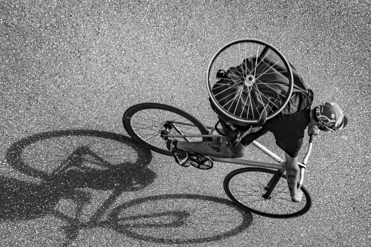 Cyclist seen from above carrying a spare wheel on his back as his shadow stretches beside him